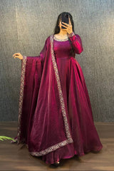 Person wearing a maroon traditional outfit with a matching dupatta against a textured wall.