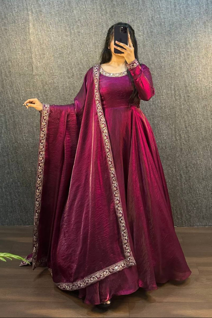 Person wearing a maroon traditional outfit with a matching dupatta against a textured wall.