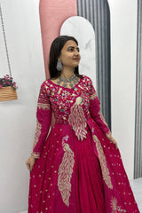 Woman wearing a pink embroidered traditional outfit in a minimal indoor setting.