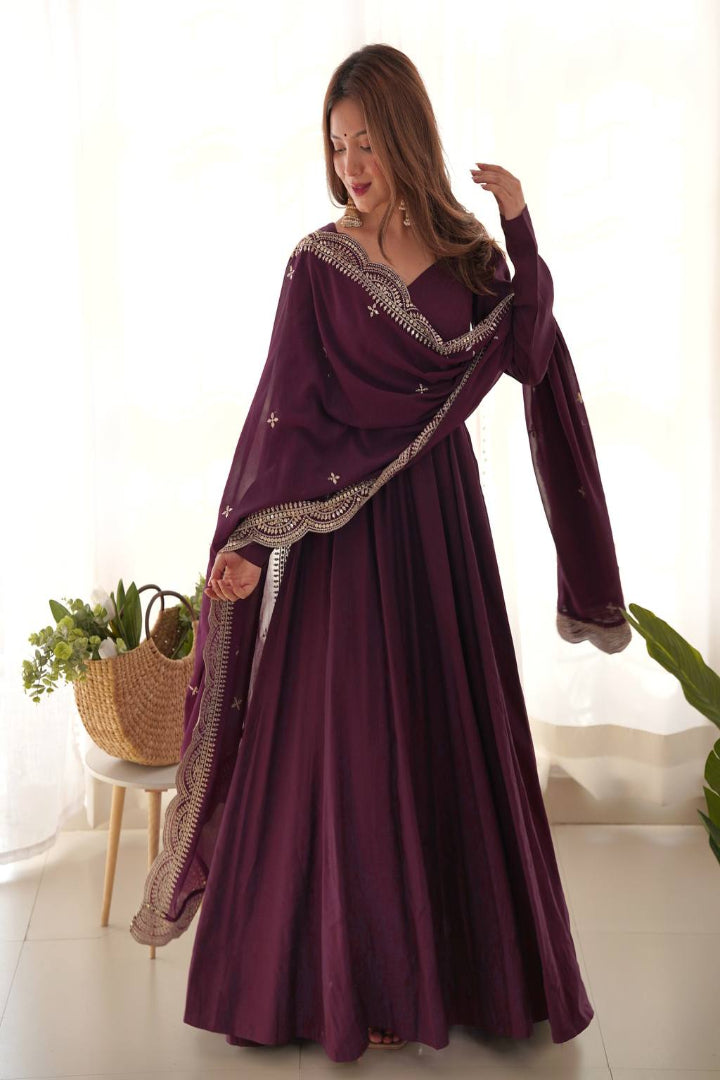 Woman wearing a long, dark purple dress with intricate detailing in a bright room.