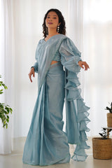 Woman wearing a light blue saree with ruffled edges in a bright room.