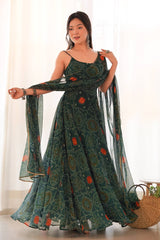 Woman wearing a long, patterned dress with a sheer dupatta, standing indoors.