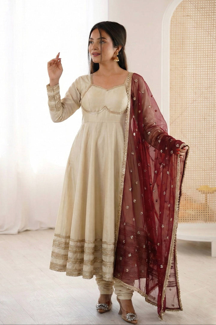 Woman in a beige traditional outfit with a red dupatta in a minimalistic room.