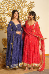 Two women modeling traditional Indian Anarkali gharara suits in a decorated indoor setting. One suit is deep blue with white polka dots and gold borders, and the other is red with white polka dots and gold borders.
