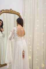 Woman in a white embroidered dress standing in front of a mirror with fairy lights.