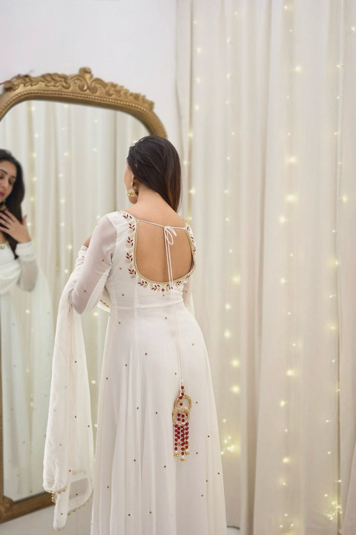 Woman in a white embroidered dress standing in front of a mirror with fairy lights.