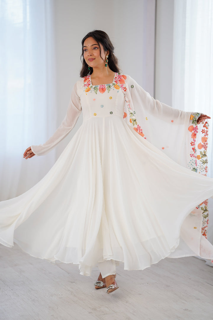 A woman modeling a flowing white traditional dress with colorful floral embroidery 